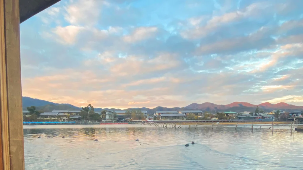 View from a wooden boat looking up the Oi River at sunset with pink and blue skies and ducks floating on the water.