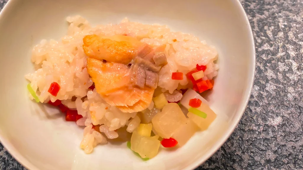 A white bowl of rice with flaked fish, pickled vegetables, and green onion.