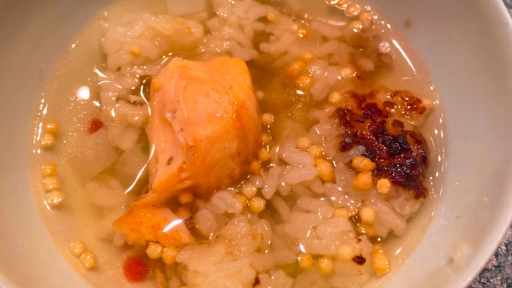 Ochazuke, the final stage of the rice course, featuring rice topped with golden dashi broth, crispy arare, and chili oil.

