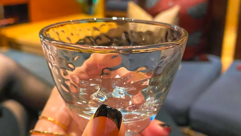 A hammered glass cocktail sitting on a dark table in the dimly lit Salon and Bar Kura.