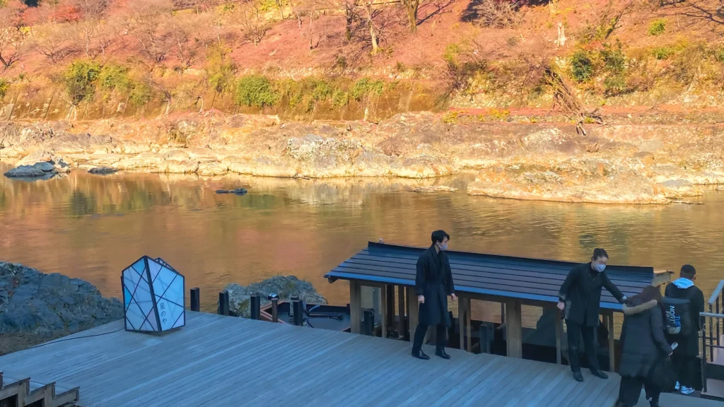 The riverside deck at Hoshinoya Kyoto with staff standing by the boat landing next to the Oi River.