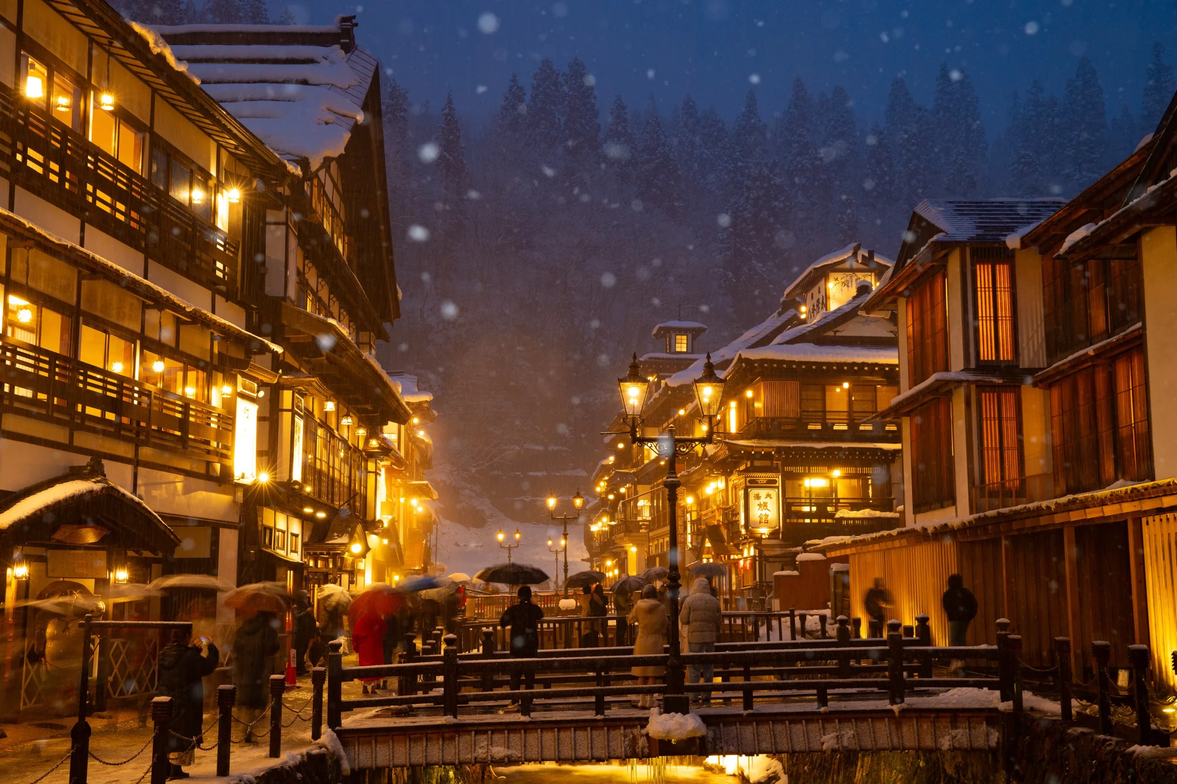 Snow falling on Ginzan Onsen at night, gas lamps illuminating Taisho-era ryokan in Yamagata