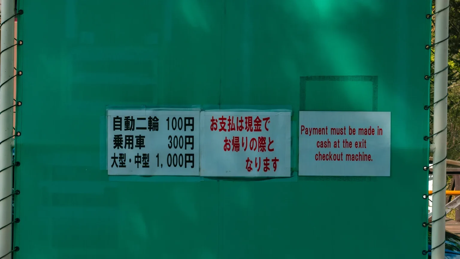 Parking fee sign at the entrance to Hana no Miyako Koen showing rates by vehicle type
