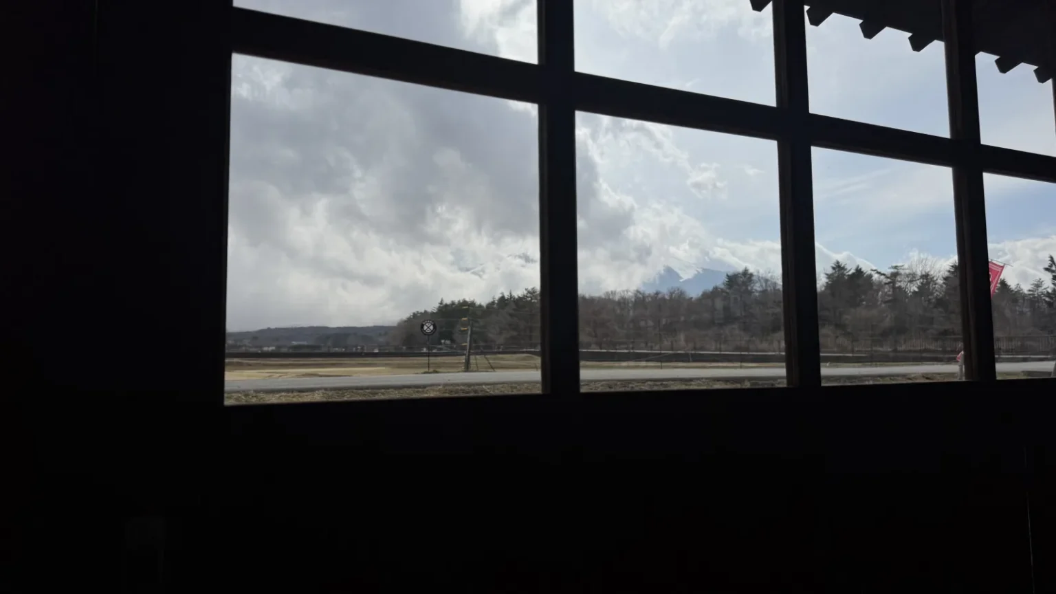 Mt. Fuji's summit completely wrapped in cap cloud, viewed through the Hanaan restaurant window — only the lower slopes visible while thick stratiform cloud sits on the peak