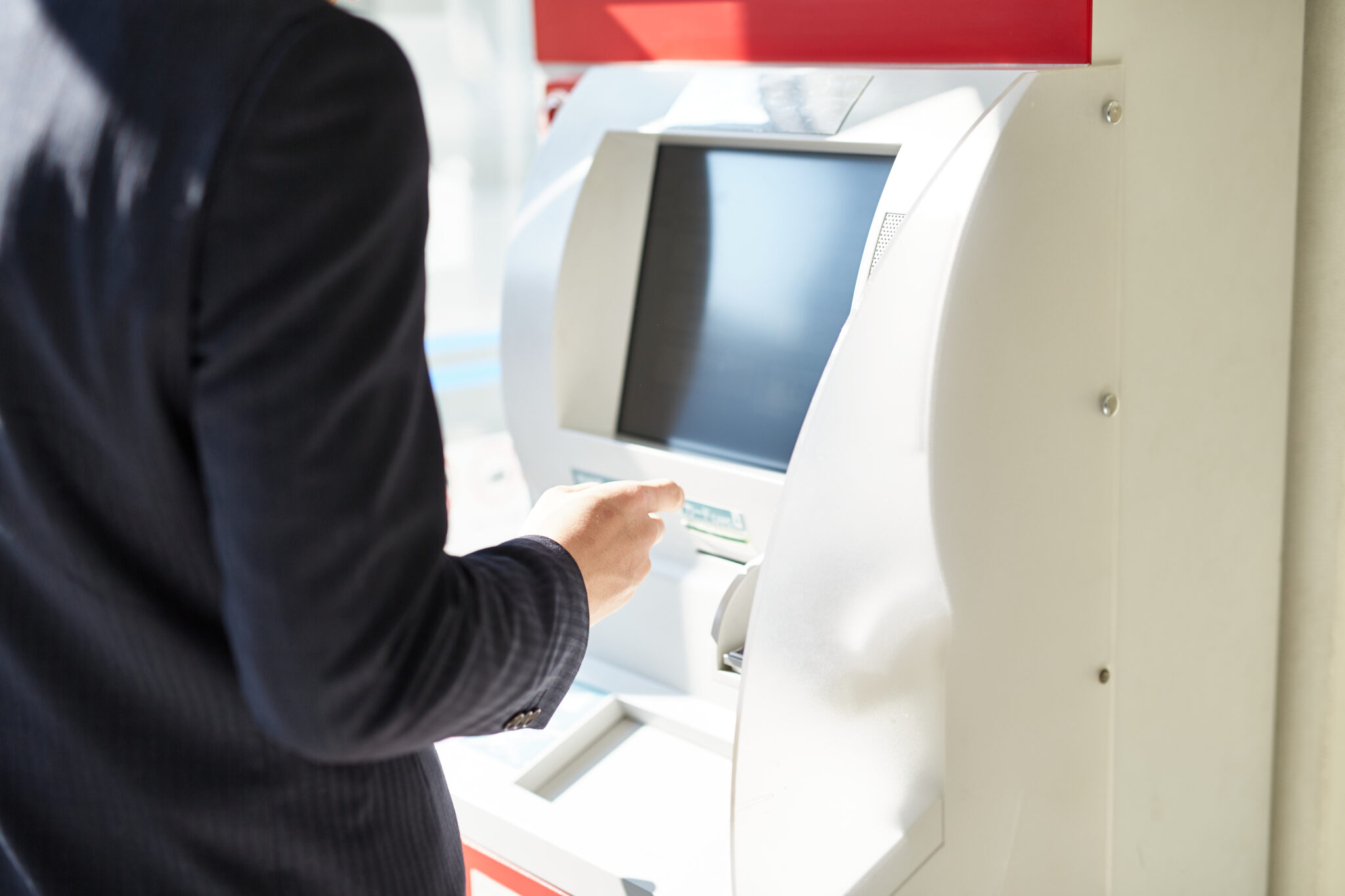 Person using a white Japanese ATM machine in a brightly lit interior