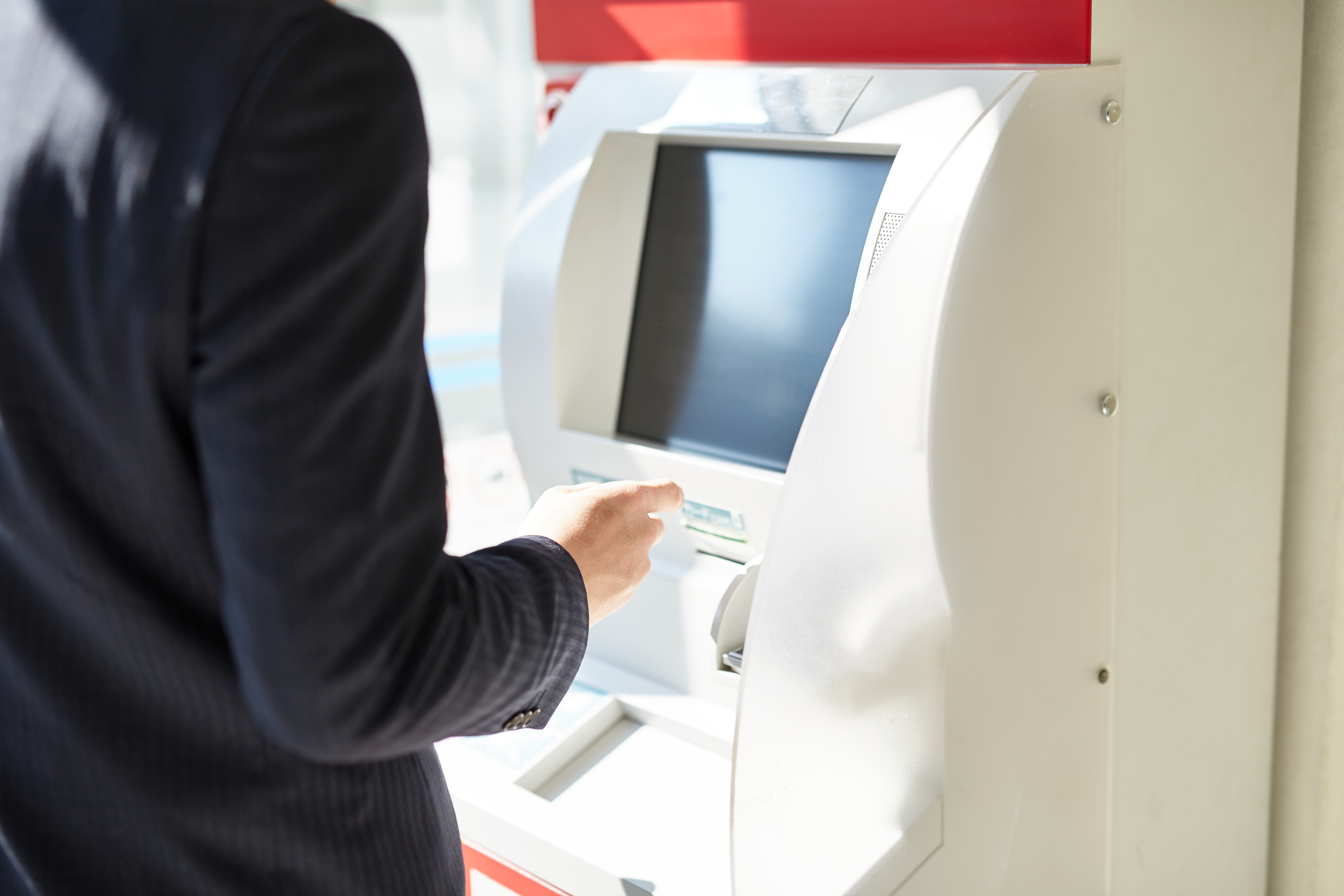 Person using a white Japanese ATM machine in a brightly lit interior