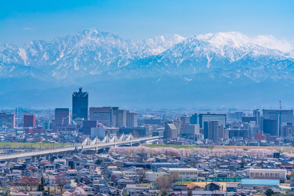 Toyama city with spring cherry blossoms in foreground and snow-capped Tateyama mountain range behind