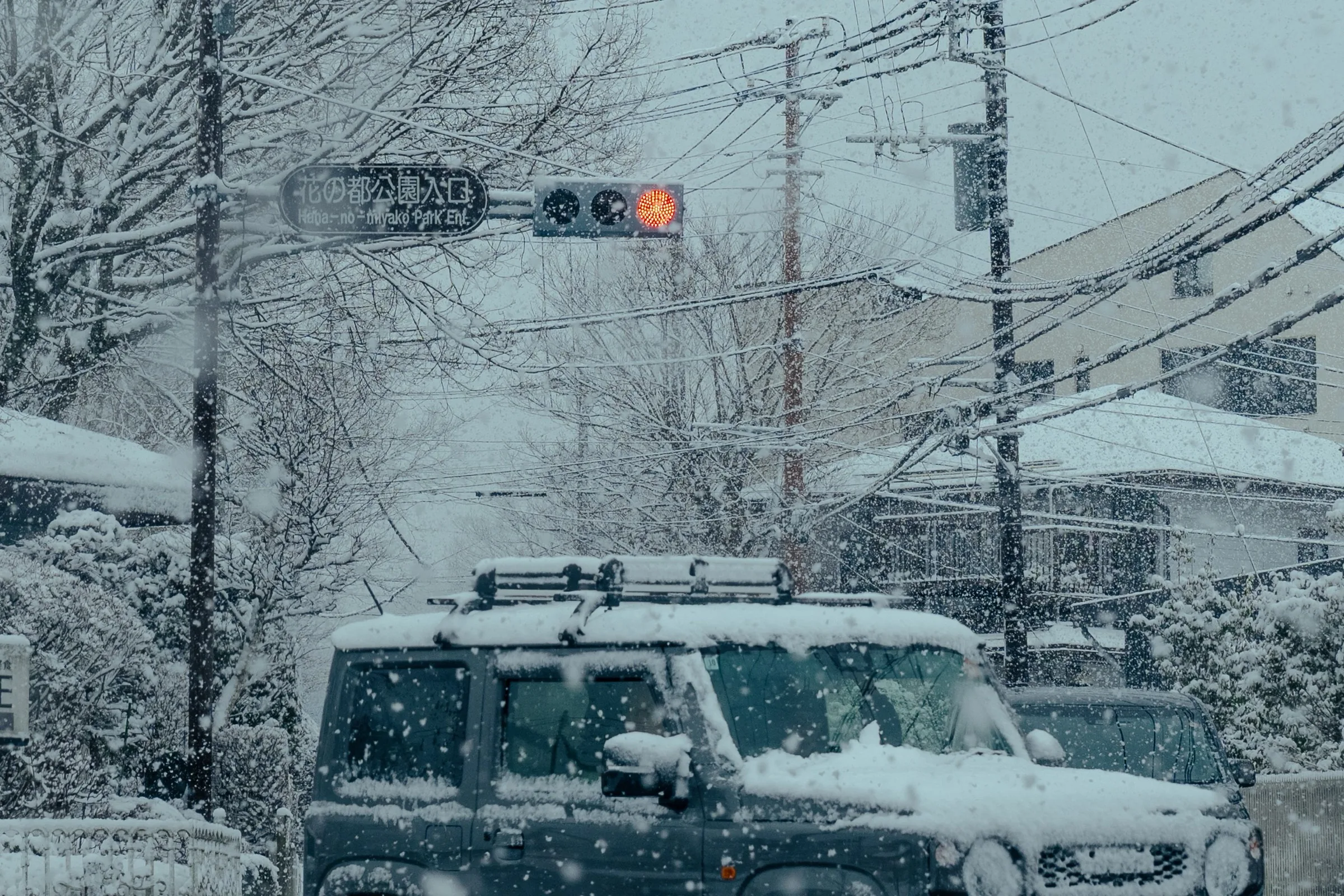 Suzuki Jimny at a residential intersection in Tokyo during a rare snow day with falling snow