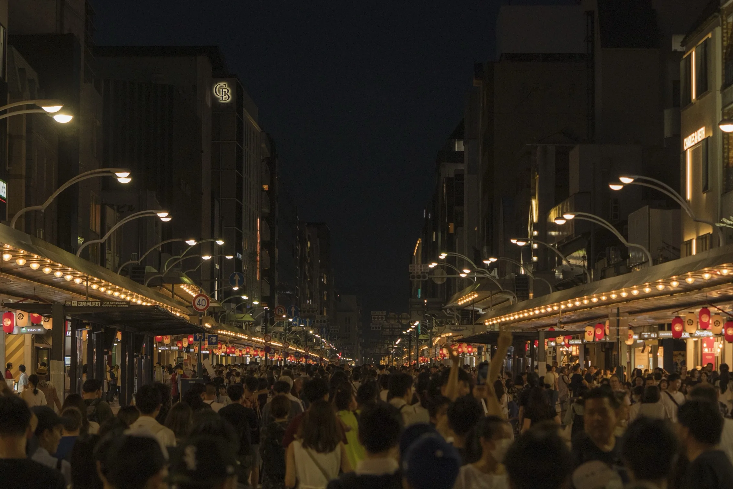 Crowd gathered on Kyoto Shijo-dori at night with lantern-lit shopping street during Gion Matsuri
