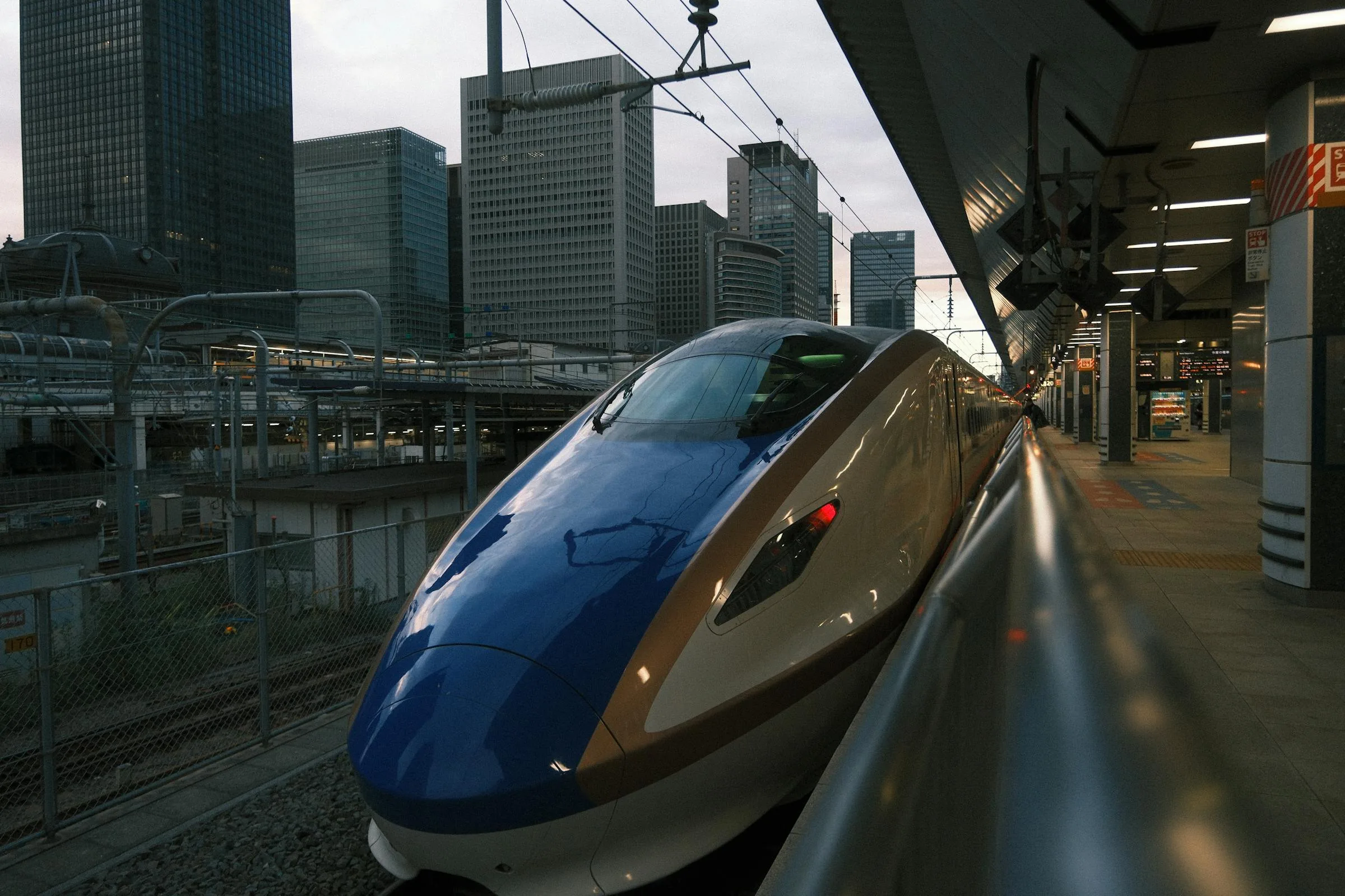 A Hokuriku shinkansen nose at Tokyo Station with the Marunouchi skyline behind, ready to head west
