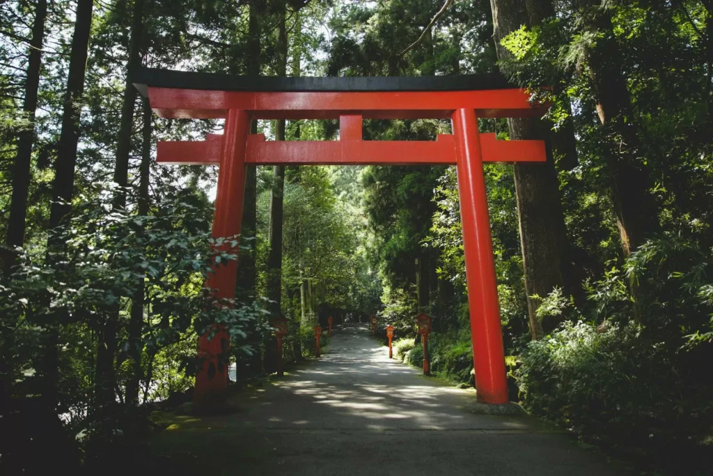 Bright red torii gate leading into a lush forested shrine approach
