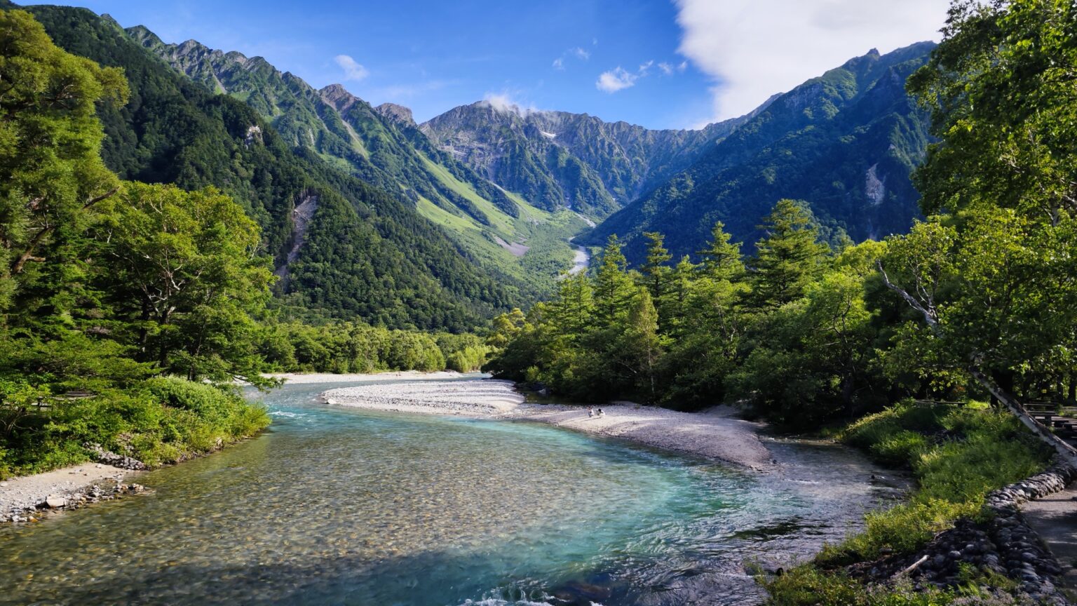 Crystal-clear Azusa River flowing through Kamikochi valley with snow-streaked Hotaka mountain range against blue summer sky