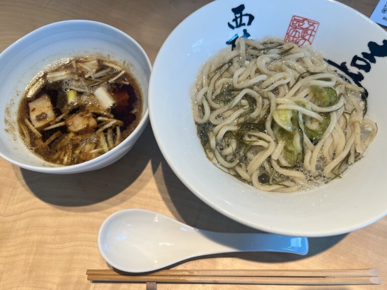 Top-down view of the kombu ramen at Kiichi: thin whole-grain noodles in clear kombu broth with shaved oboro kombu, alongside a small dipping bowl, ceramic spoon and bamboo chopsticks