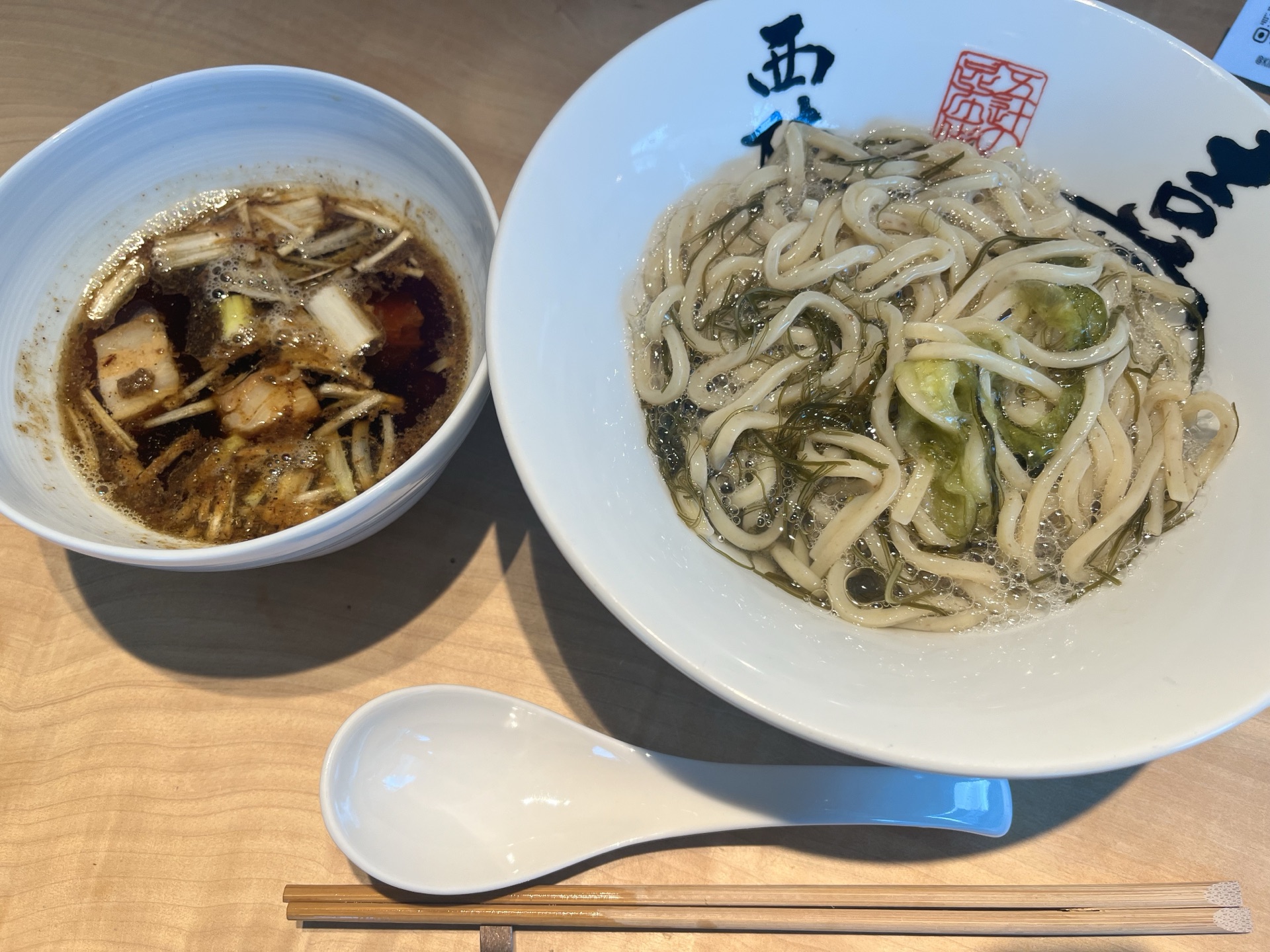 Top-down view of the kombu ramen at Kiichi: thin whole-grain noodles in clear kombu broth with shaved oboro kombu, alongside a small dipping bowl, ceramic spoon and bamboo chopsticks