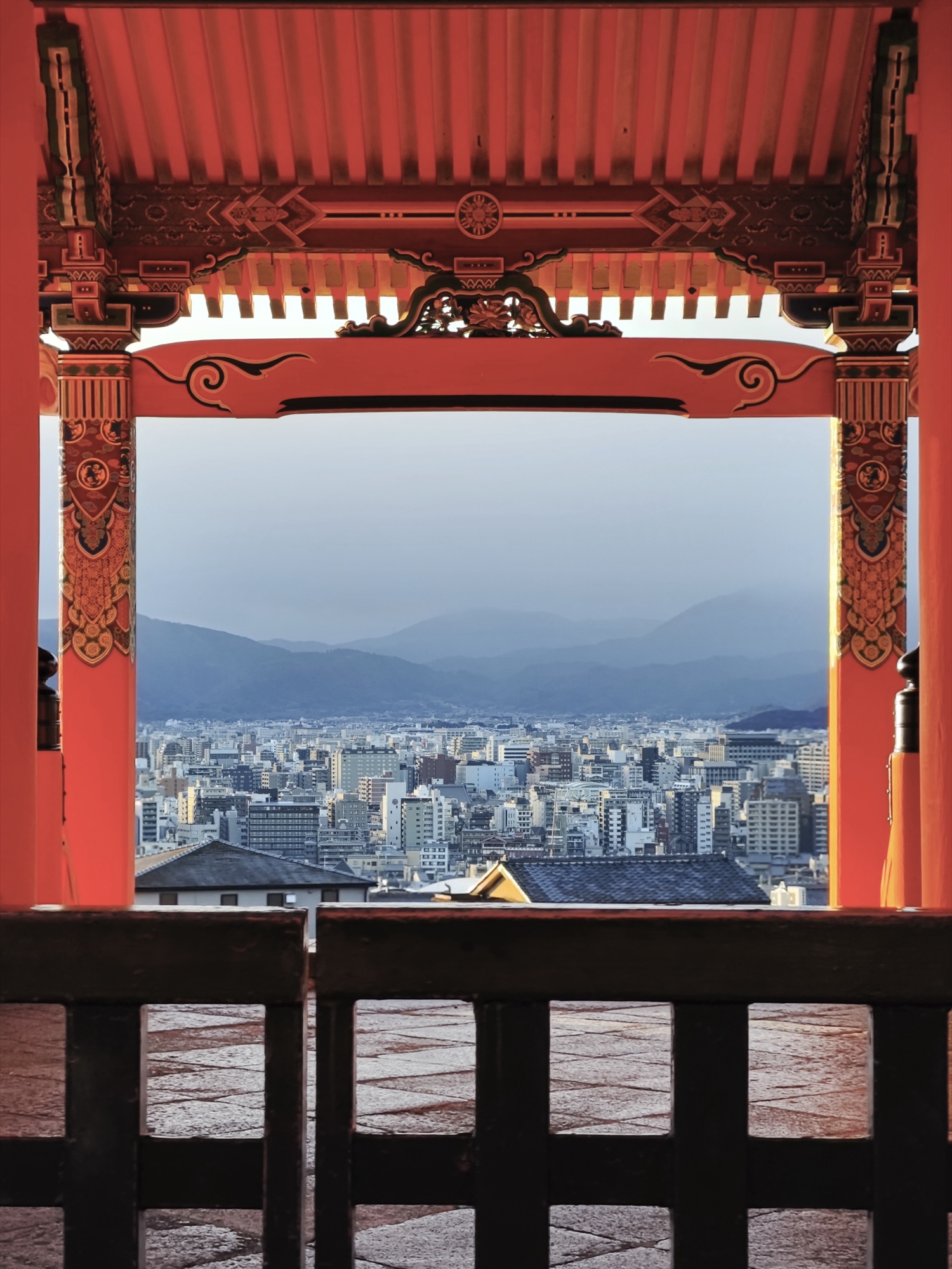 Kyoto city skyline framed through vermilion columns of Kiyomizudera Nishi-mon West Gate