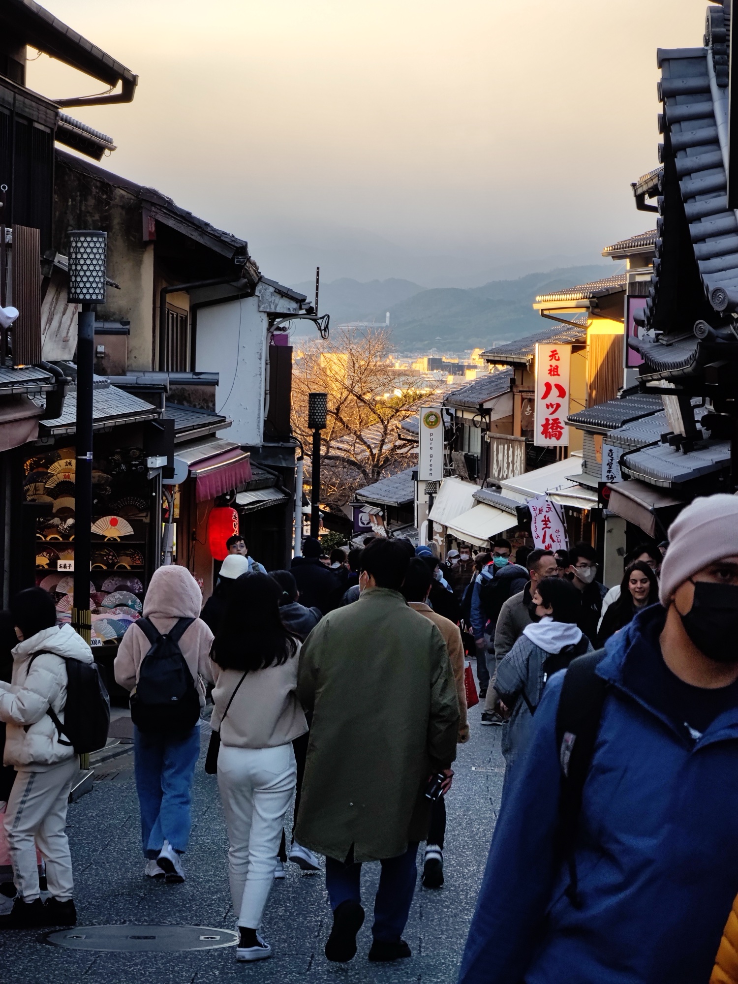 Crowd walking through Ninenzaka with traditional shops and distant mountains in Kyoto Higashiyama