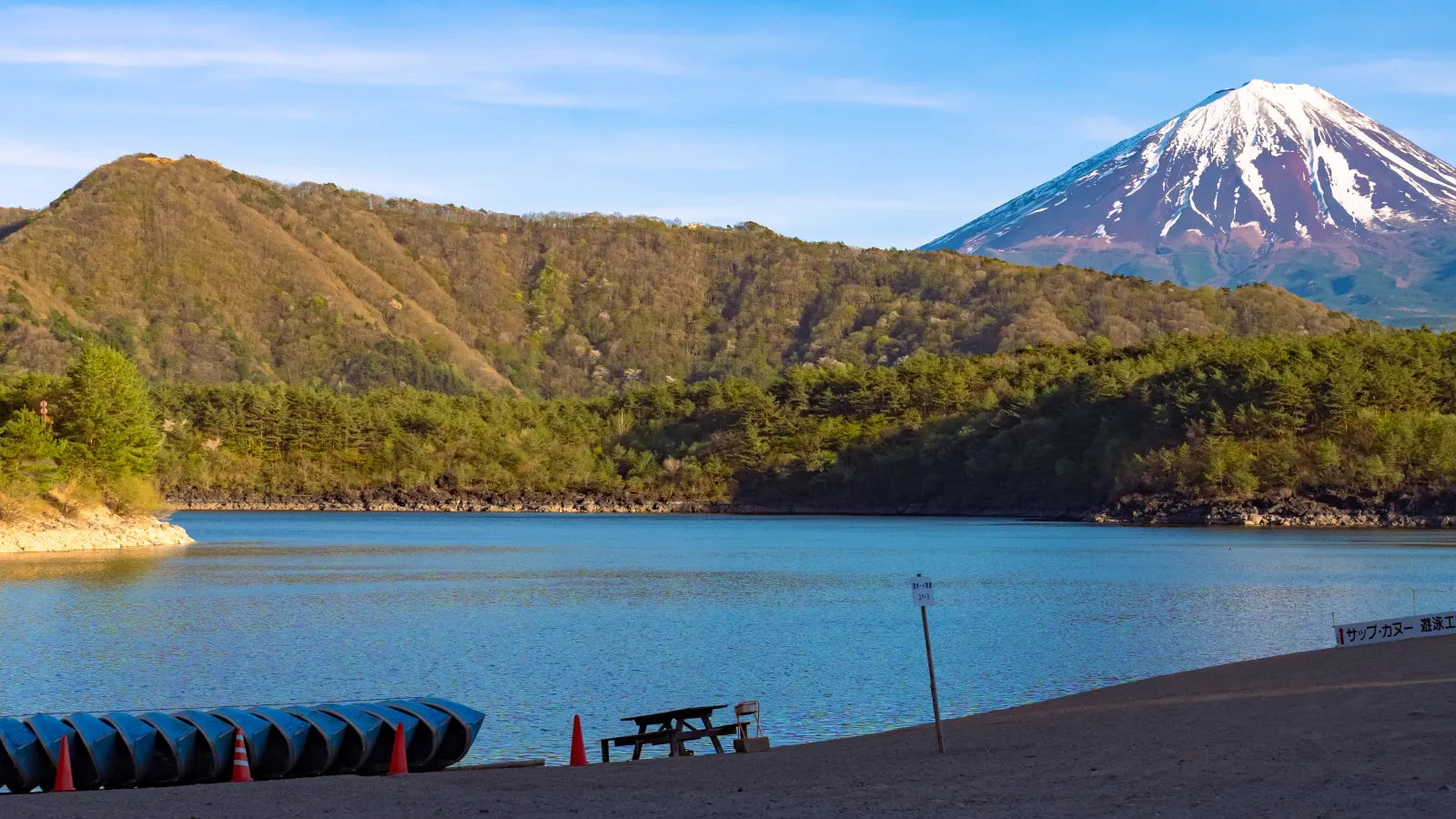Beach with stacked canoes at Lake Saiko with Mt Fuji visible behind hills