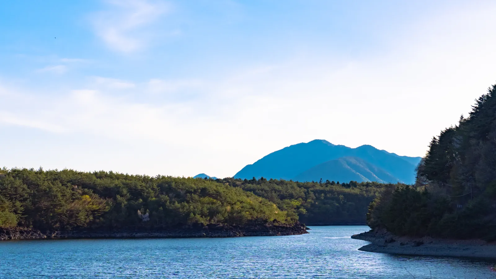 Moody shoreline view of Lake Saiko with forested hills