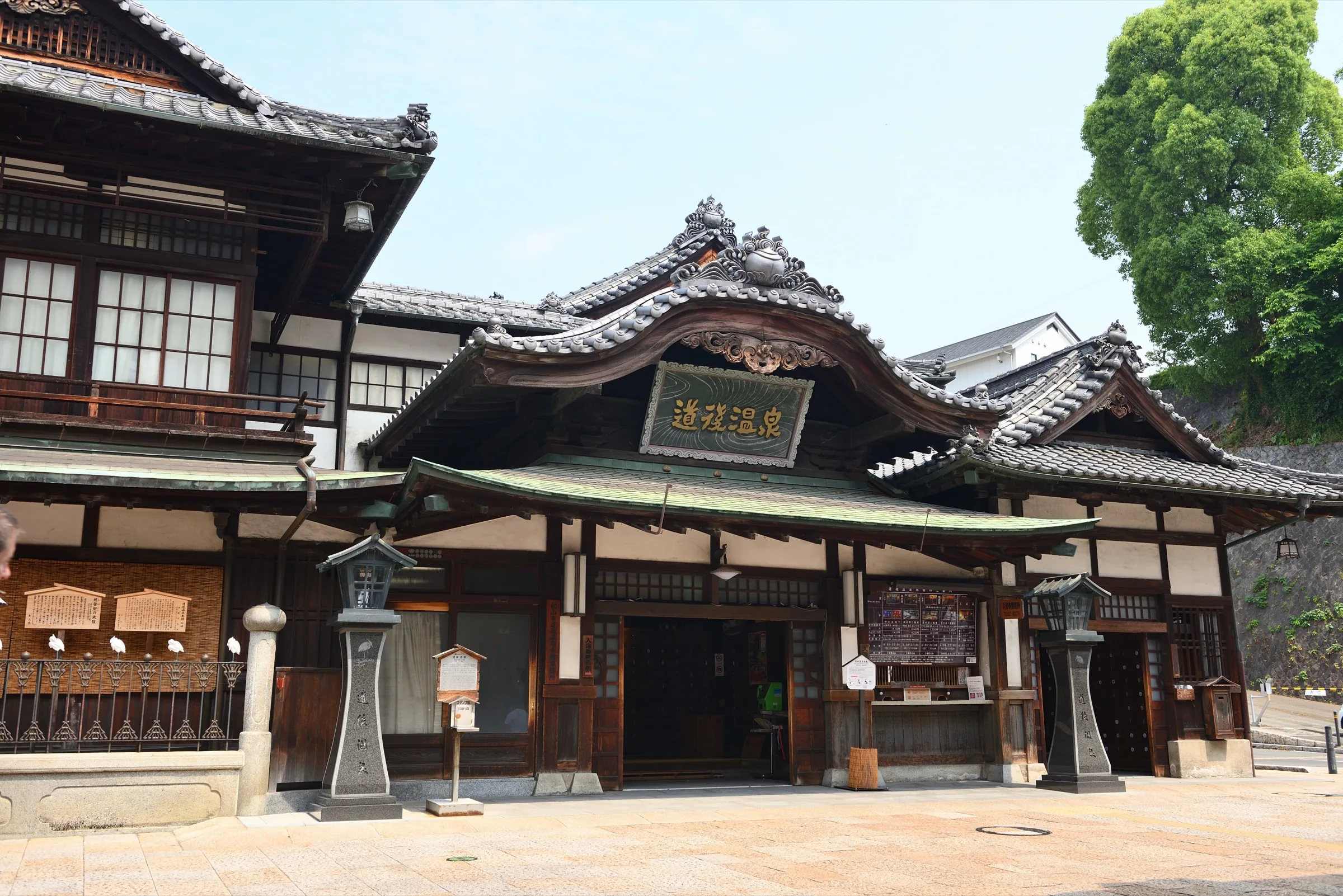 Wooden three-story Dogo Onsen Honkan bathhouse facade with traditional curved gable roof in Matsuyama