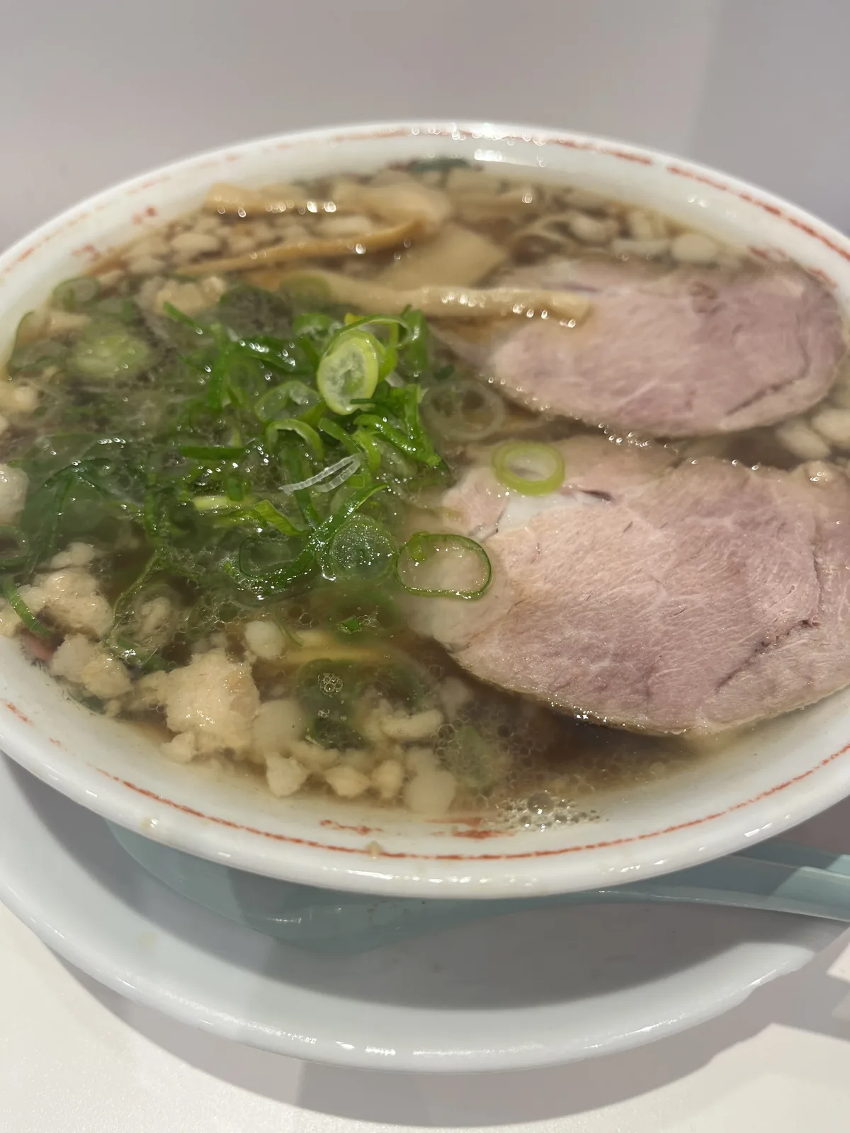 Close-up of Onomichi ramen showing soy-based broth, two thick chashu pork slices, scallions, and the floating chunks of pork back fat that define the local style