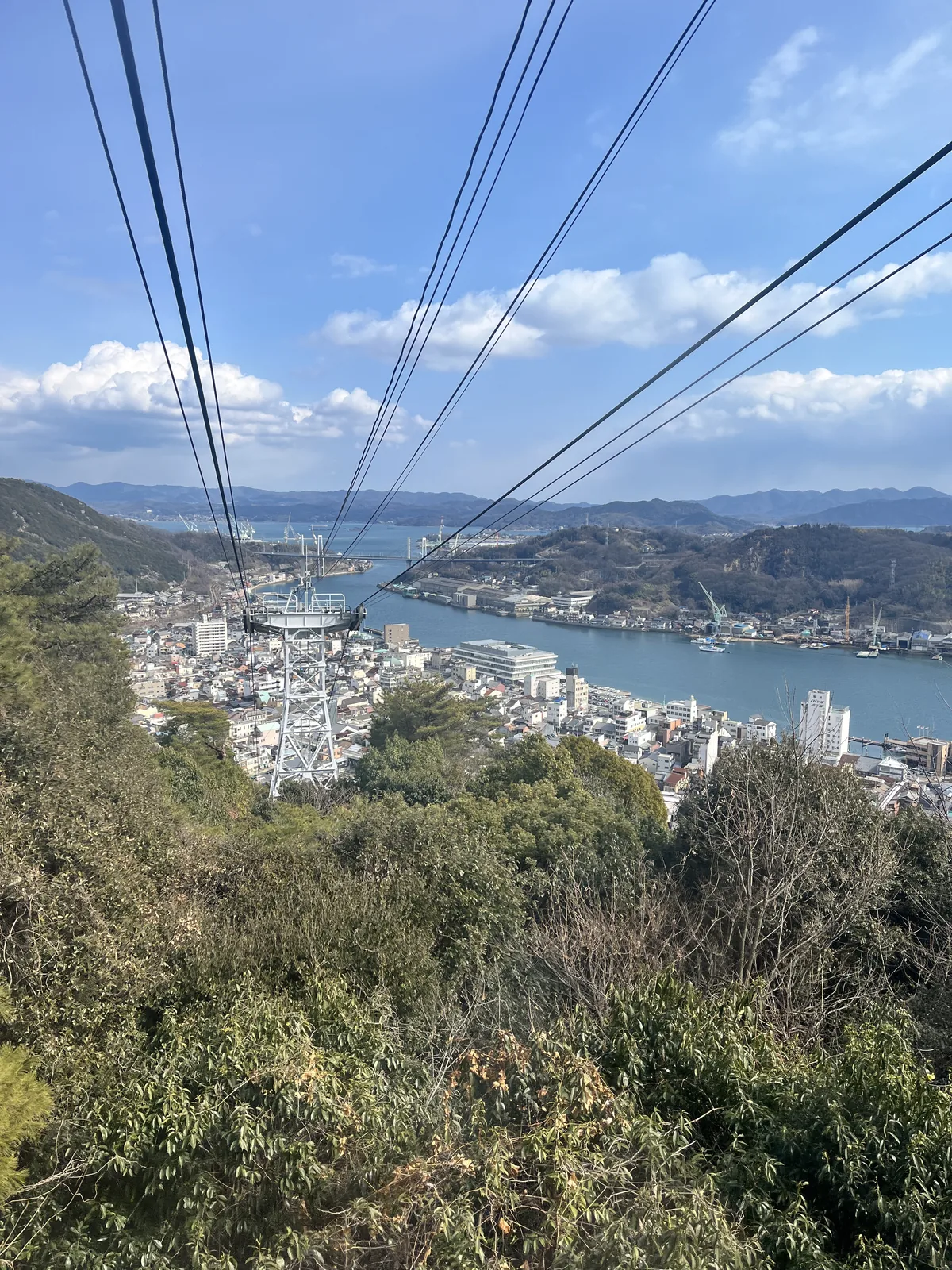 View from inside the Onomichi Ropeway gondola descending the hillside, with the channel and Shin-Onomichi Bridge visible across the water
