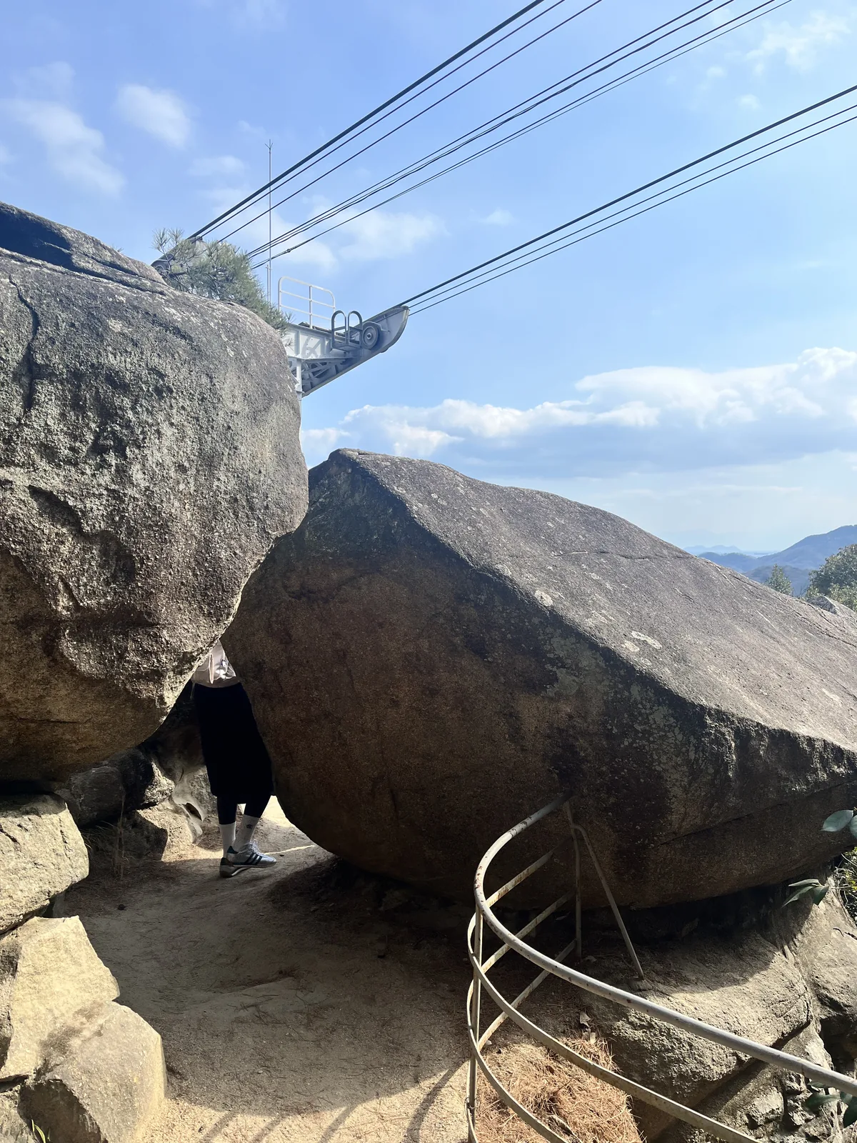 The giant balanced boulders above Senkoji Temple in Onomichi, with the temple ropeway cables visible above and a small visitor below for scale