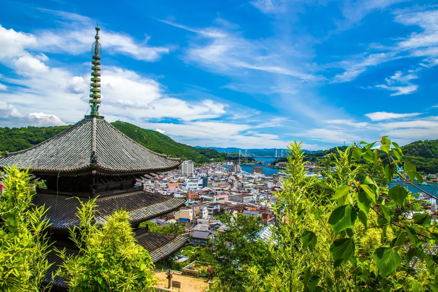Onomichi panorama from Senkoji Temple — the three-storied pagoda of Tenneiji on the left, the town spread below, the Onomichi Channel and Mukaishima island, with Shin-Onomichi Bridge in the distance