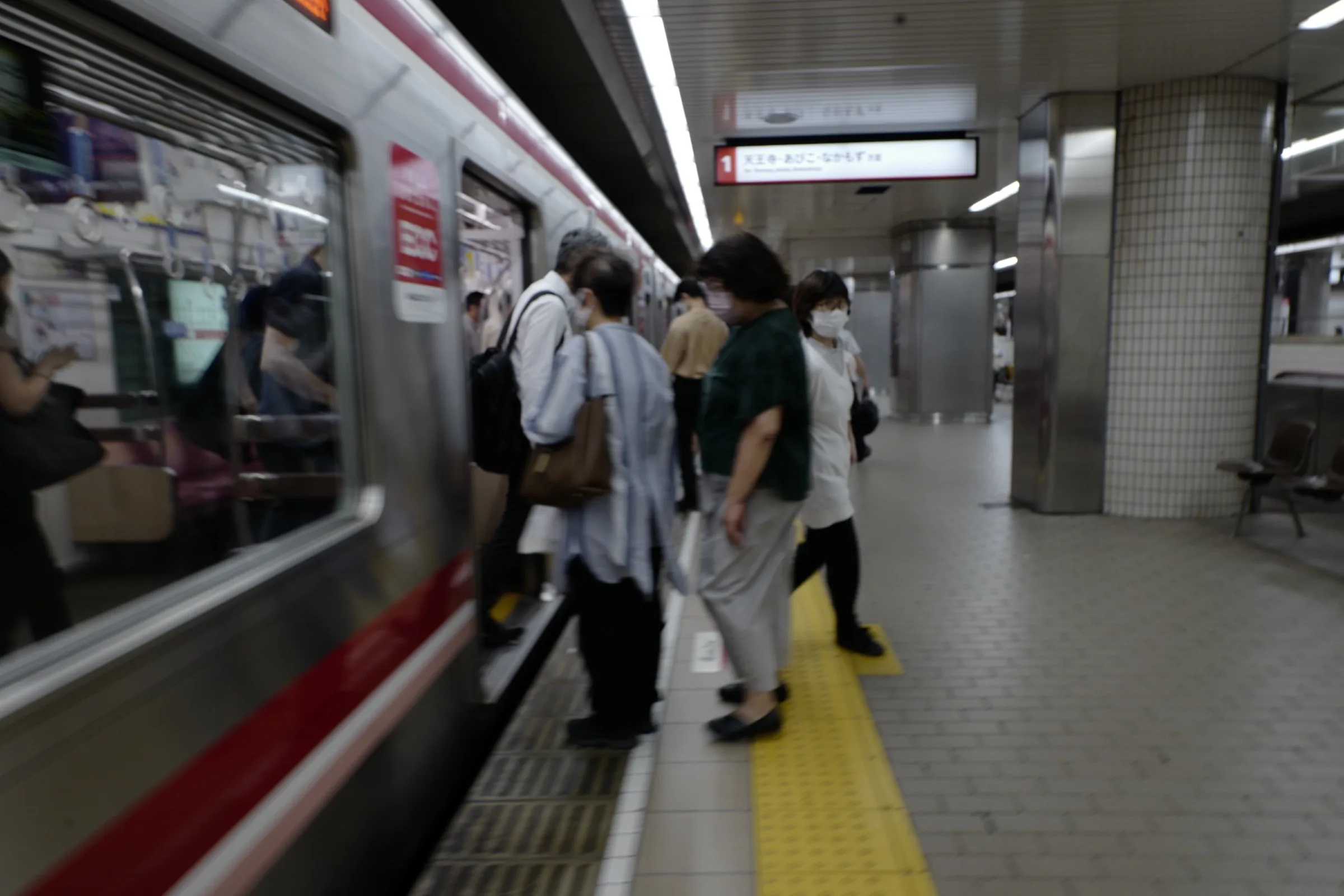 Commuters boarding a red-striped Osaka Metro Midosuji Line train at a tiled platform