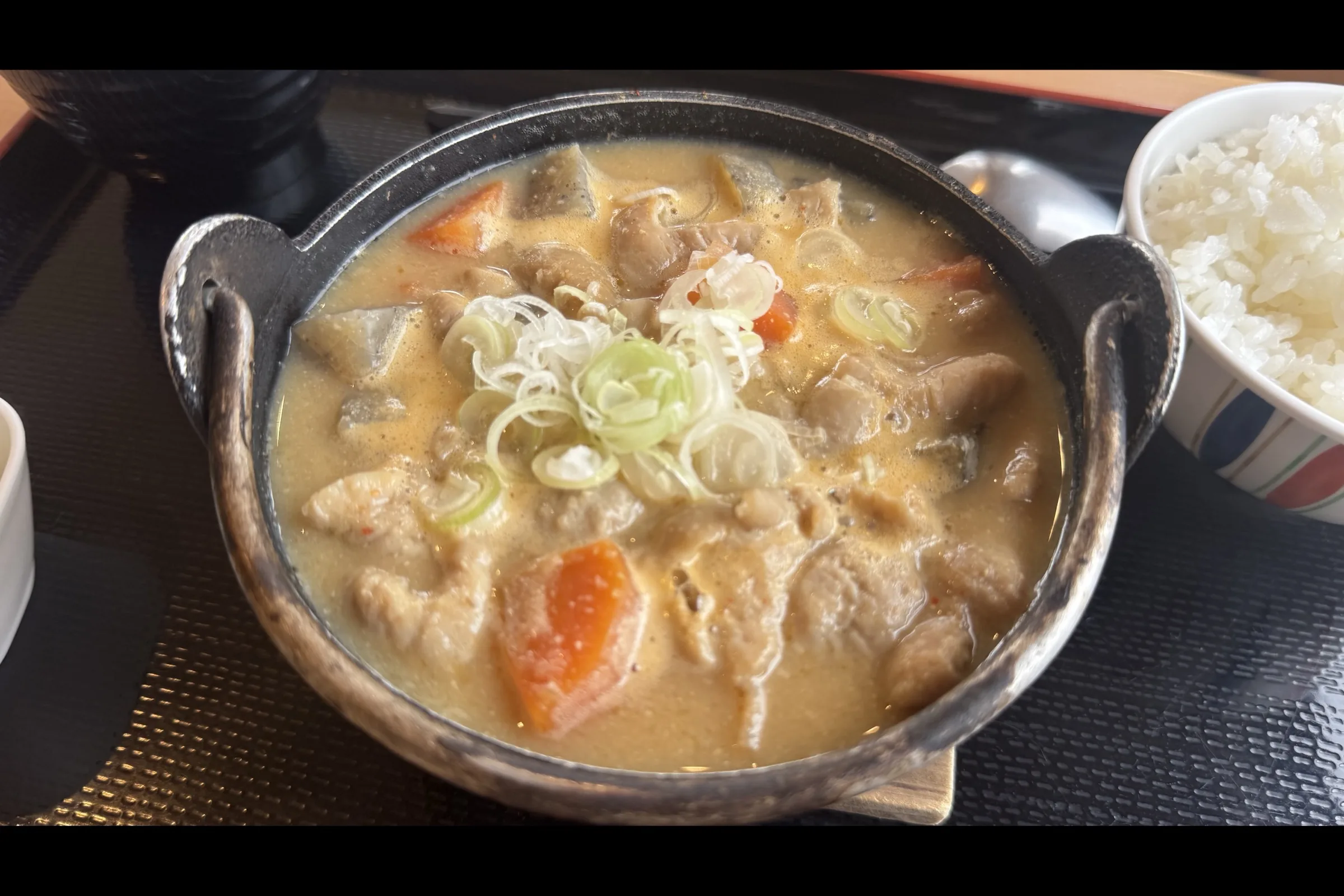 Close-up of motsu-nikomi in an iron pot with white scallions and orange carrots