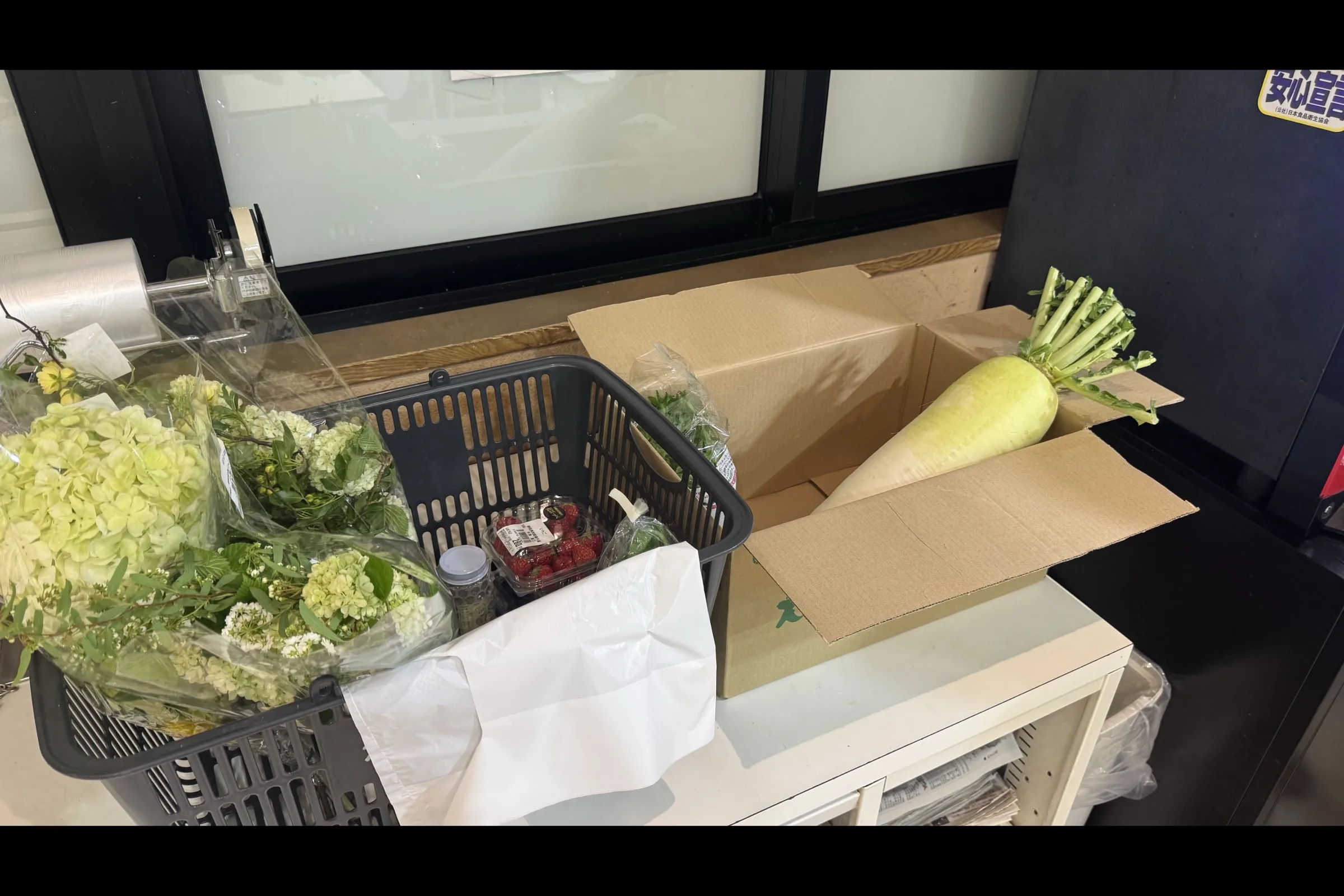 Shopping basket at checkout containing fresh daikon radish, a hydrangea bouquet, and strawberries from Michi-no-Eki Fujioyama