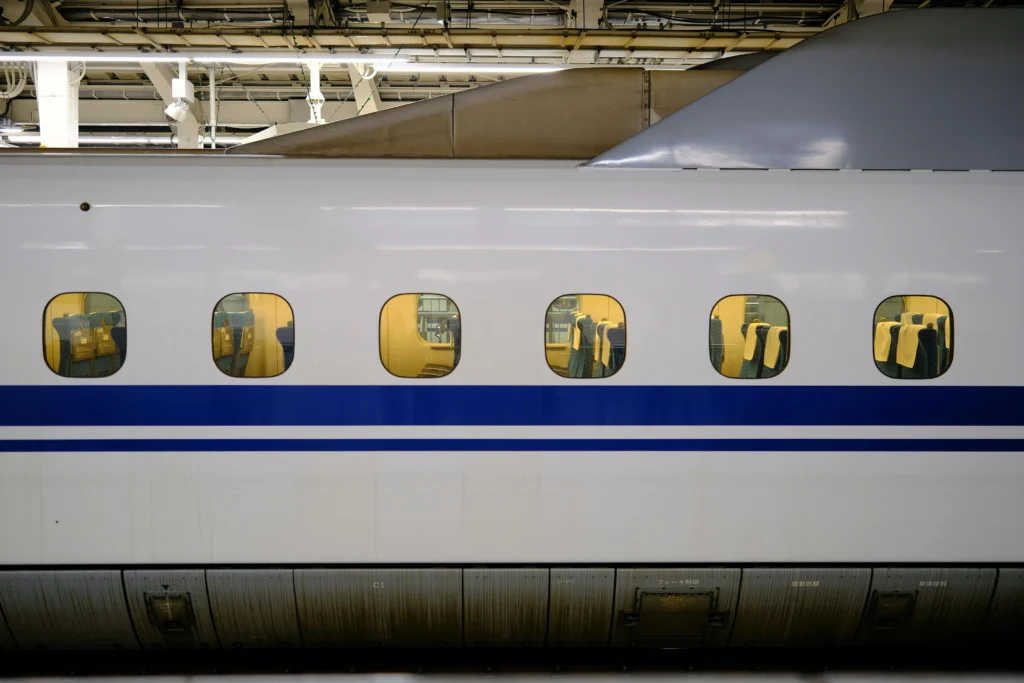A Tokaido Shinkansen bullet train at a station platform, showing the iconic white body with blue stripe and yellow reserved seats through the windows.