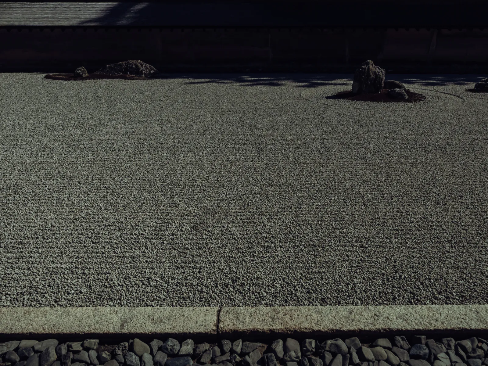 Minimalist view of raked gravel and two rocks in the Ryoanji garden