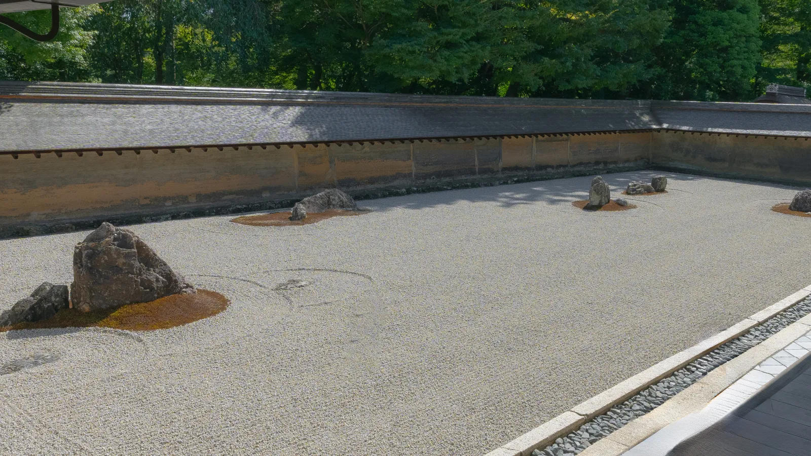 Ryoanji rock garden full view with raked gravel rocks and earthen wall in Kyoto