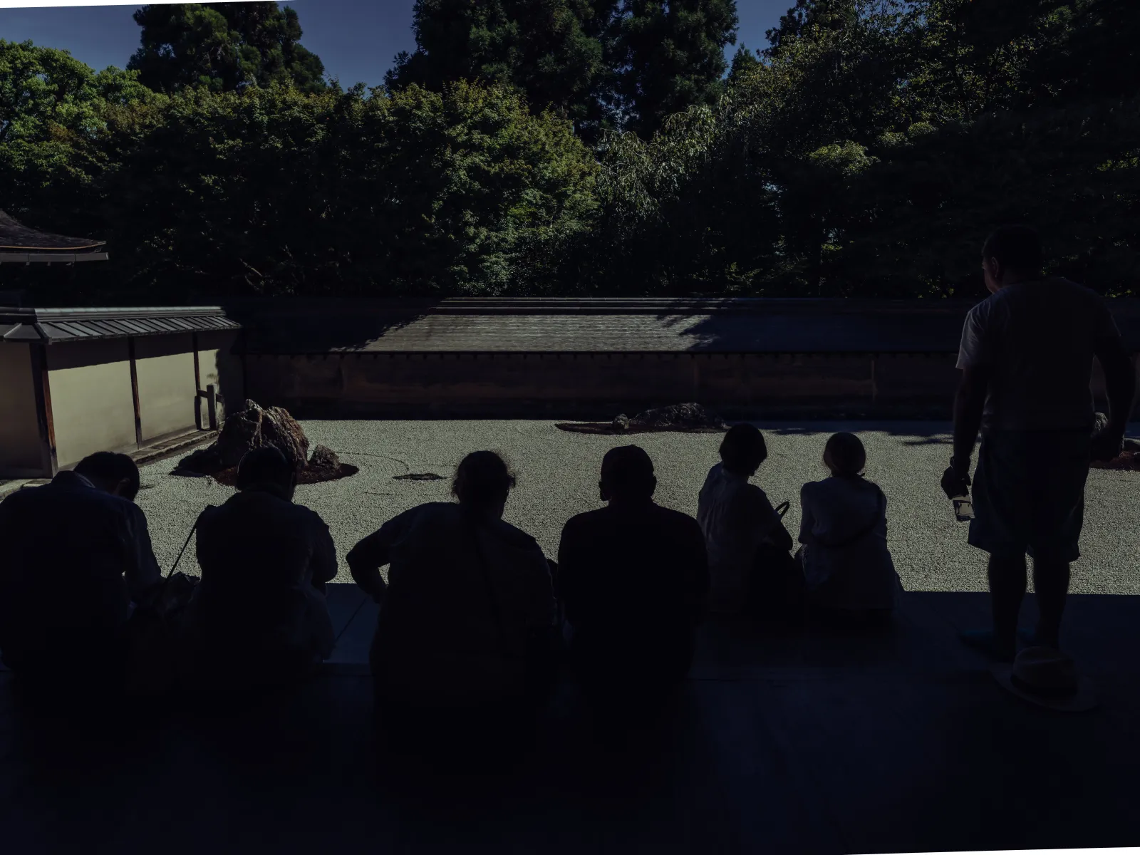 Silhouettes of visitors contemplating the Ryoanji rock garden in late afternoon light