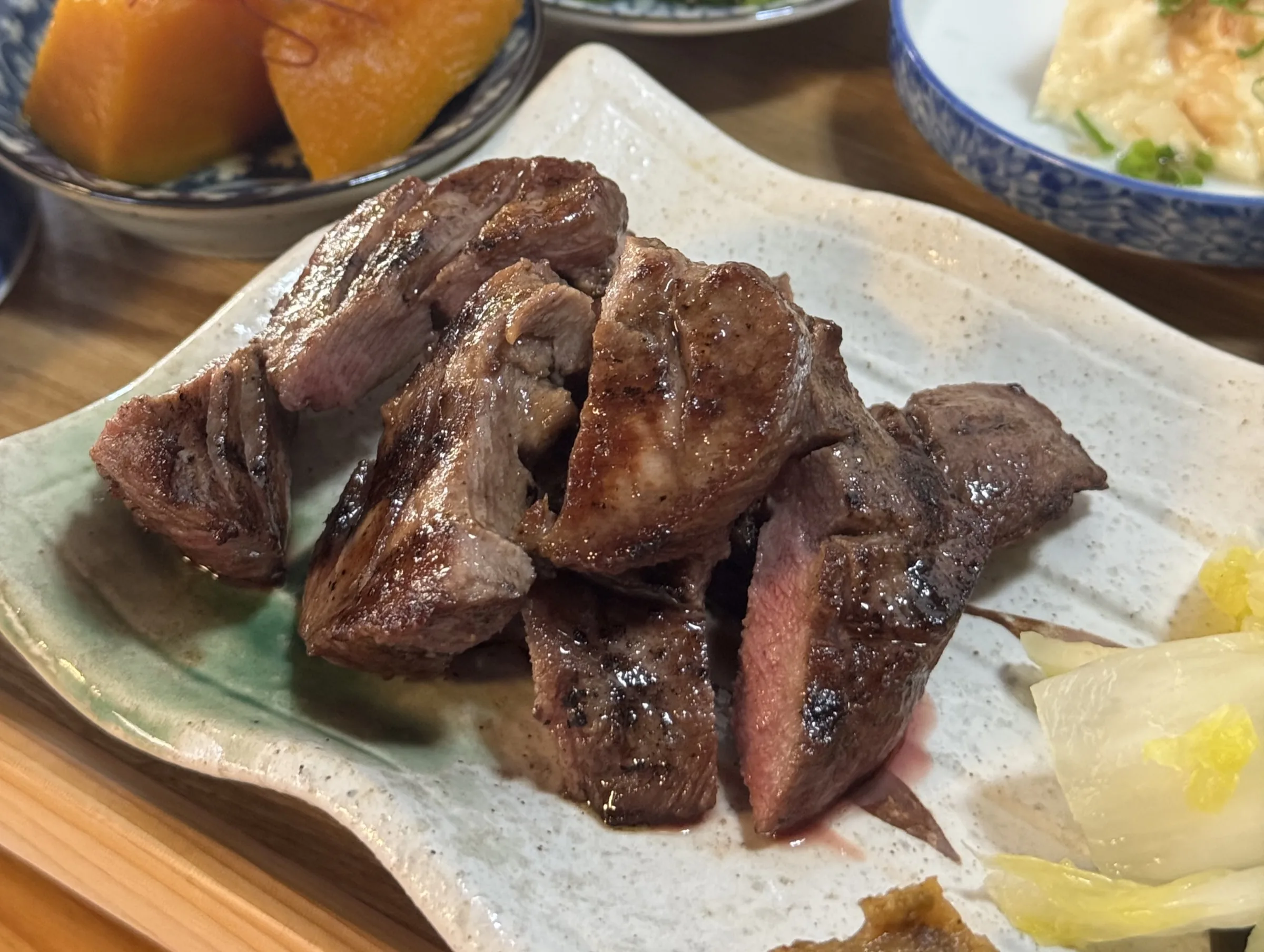 Charcoal-grilled gyutan beef tongue thick-sliced and arranged on a green ceramic plate with squash and pickles, the Sendai specialty