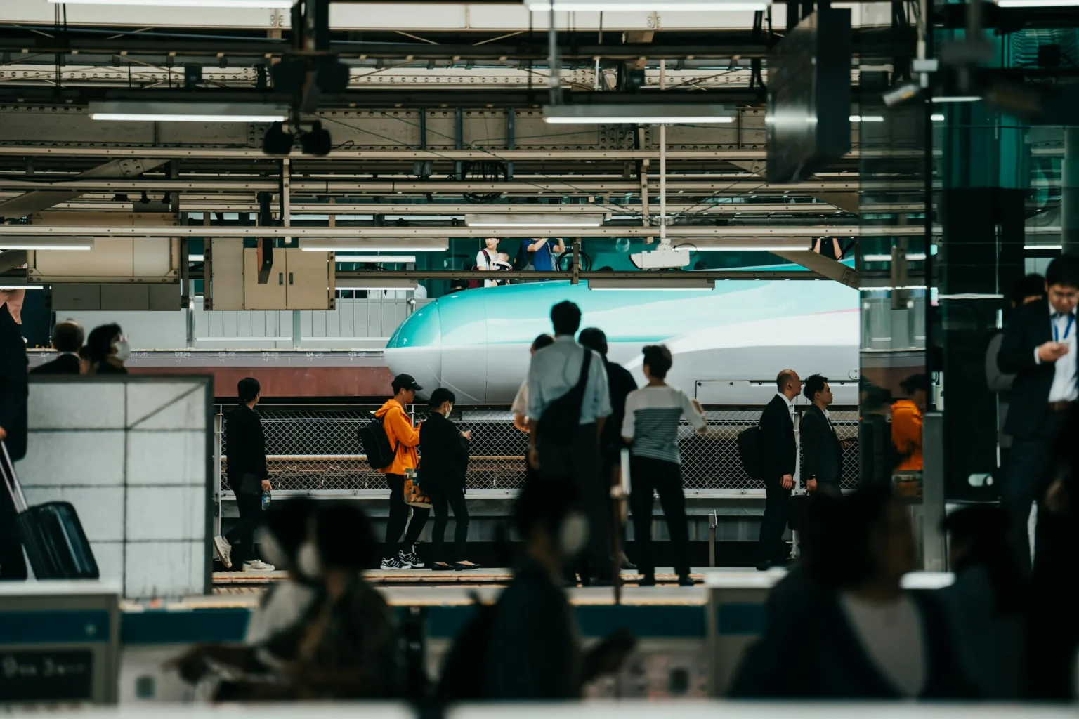 Crowd of travelers waiting on a Tokyo Station platform as a green Hayabusa shinkansen stops beside them