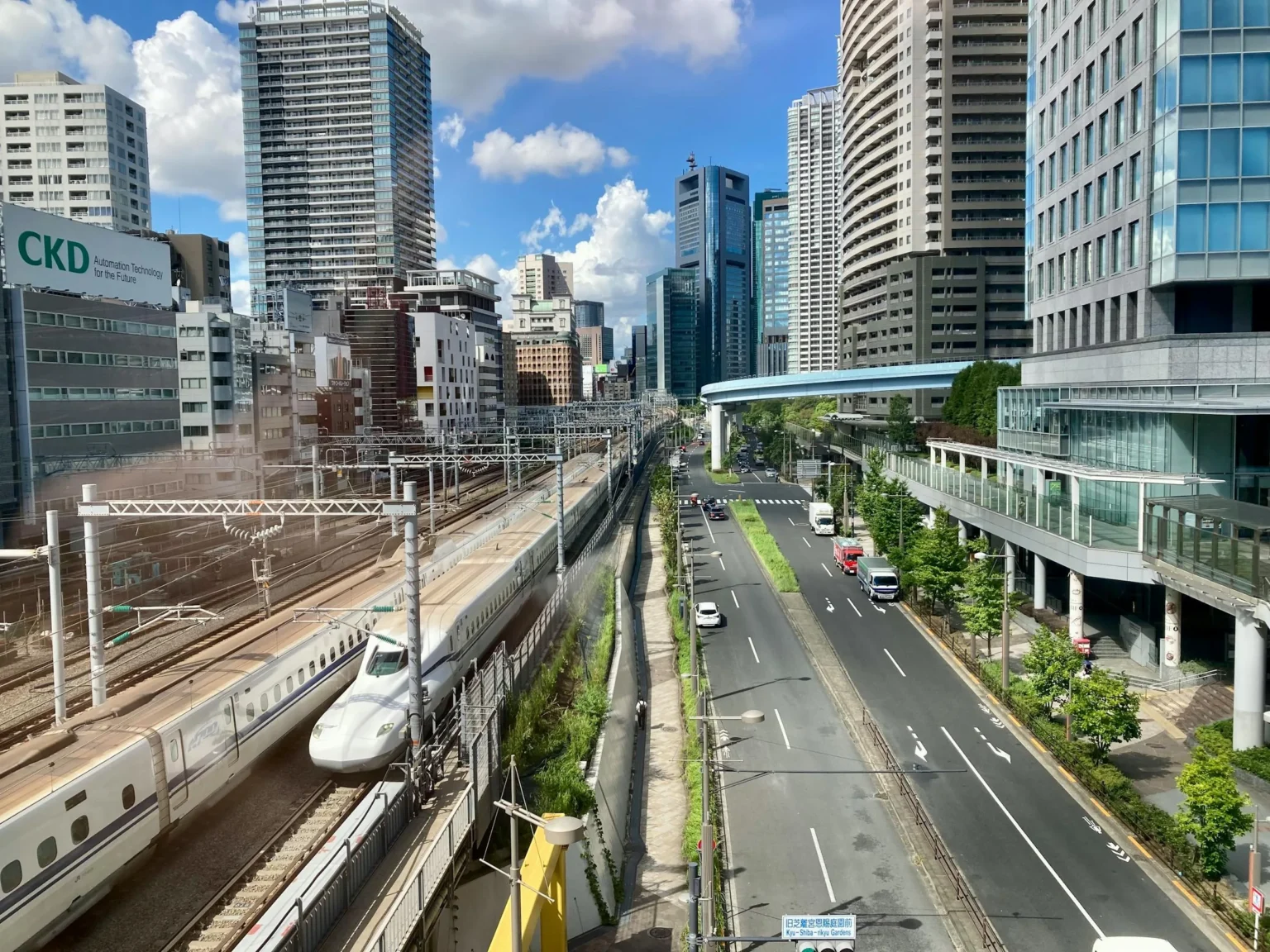 N700 shinkansen passing below Tokyo skyscrapers with highway and street beneath