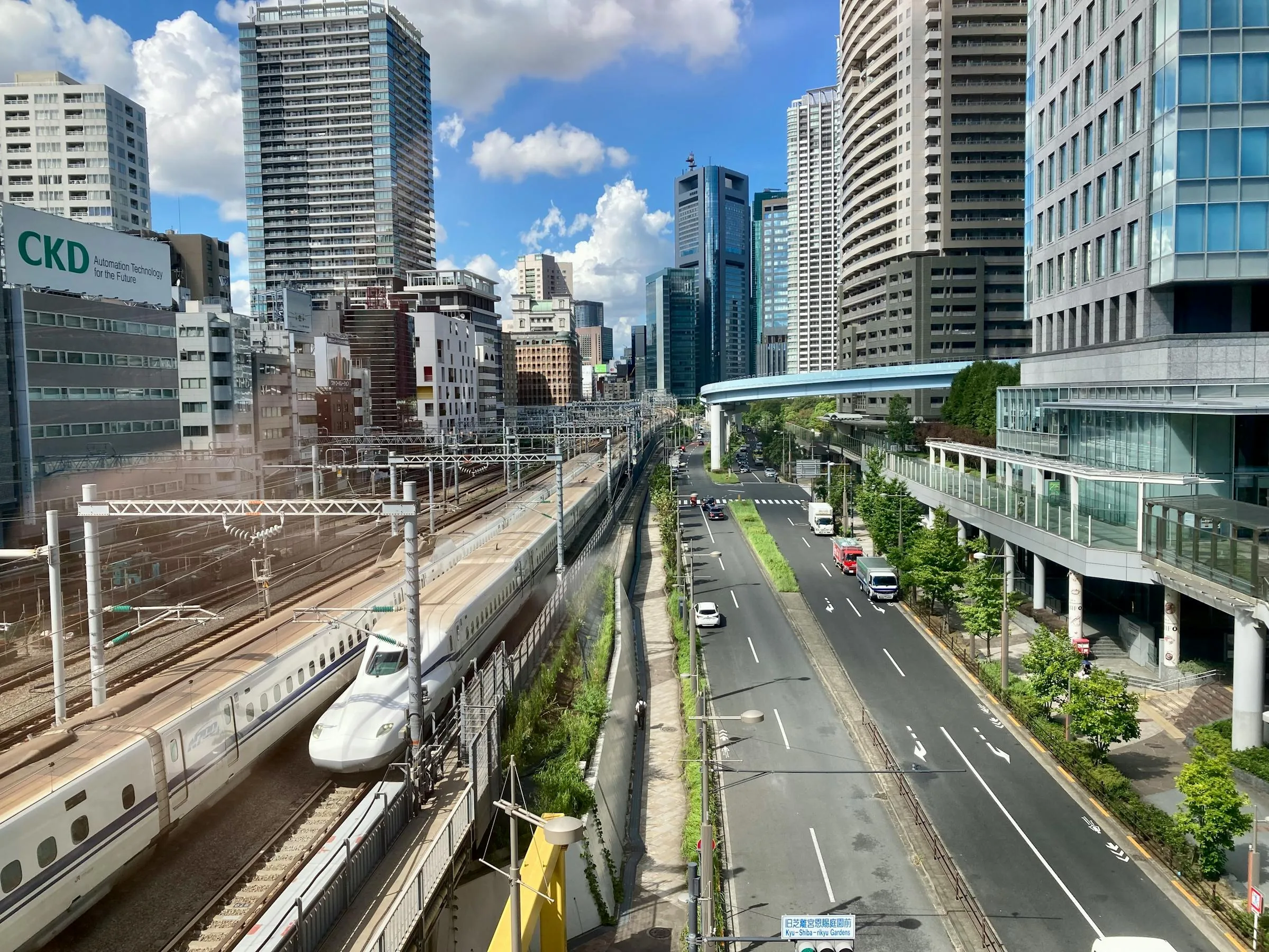 N700 shinkansen passing below Tokyo skyscrapers with highway and street beneath