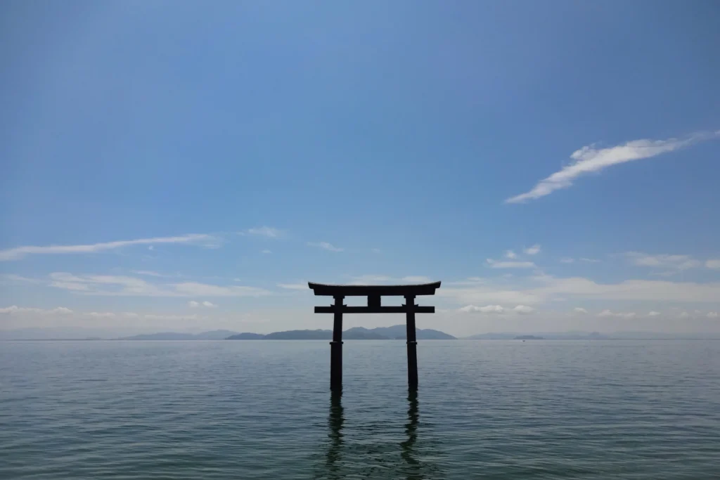 Vermillion Shirahige Shrine torii standing in Lake Biwa with calm water and distant mountains