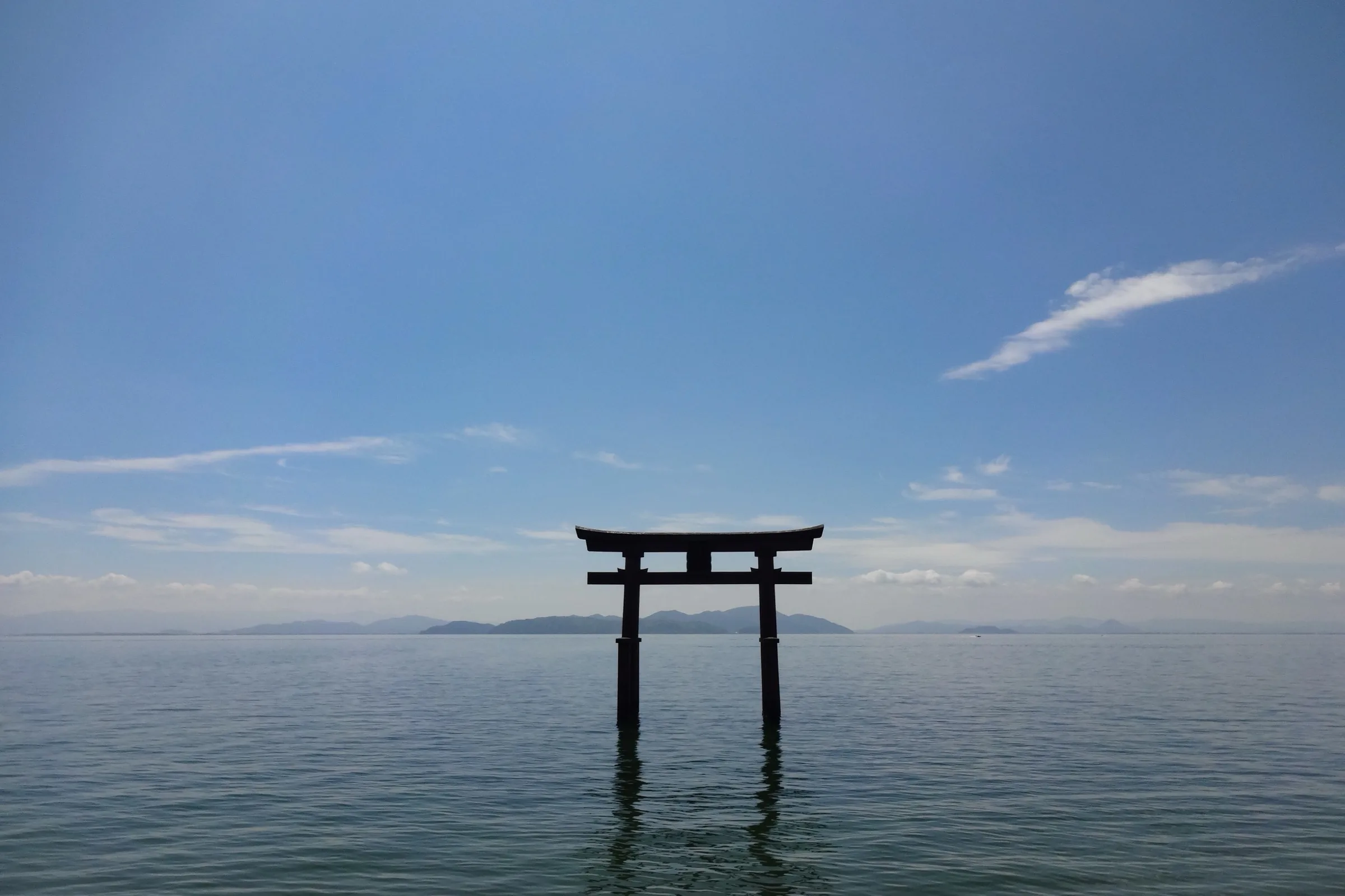 Vermillion Shirahige Shrine torii standing in Lake Biwa with calm water and distant mountains