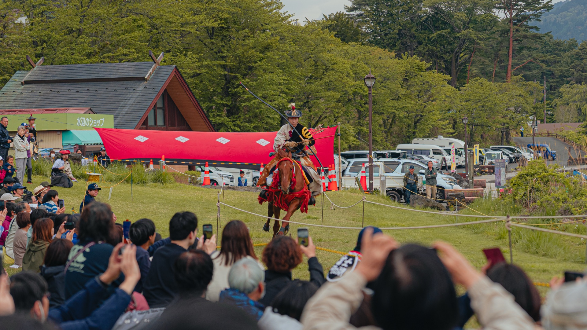 Galloping yabusame archer with audience holding up phones