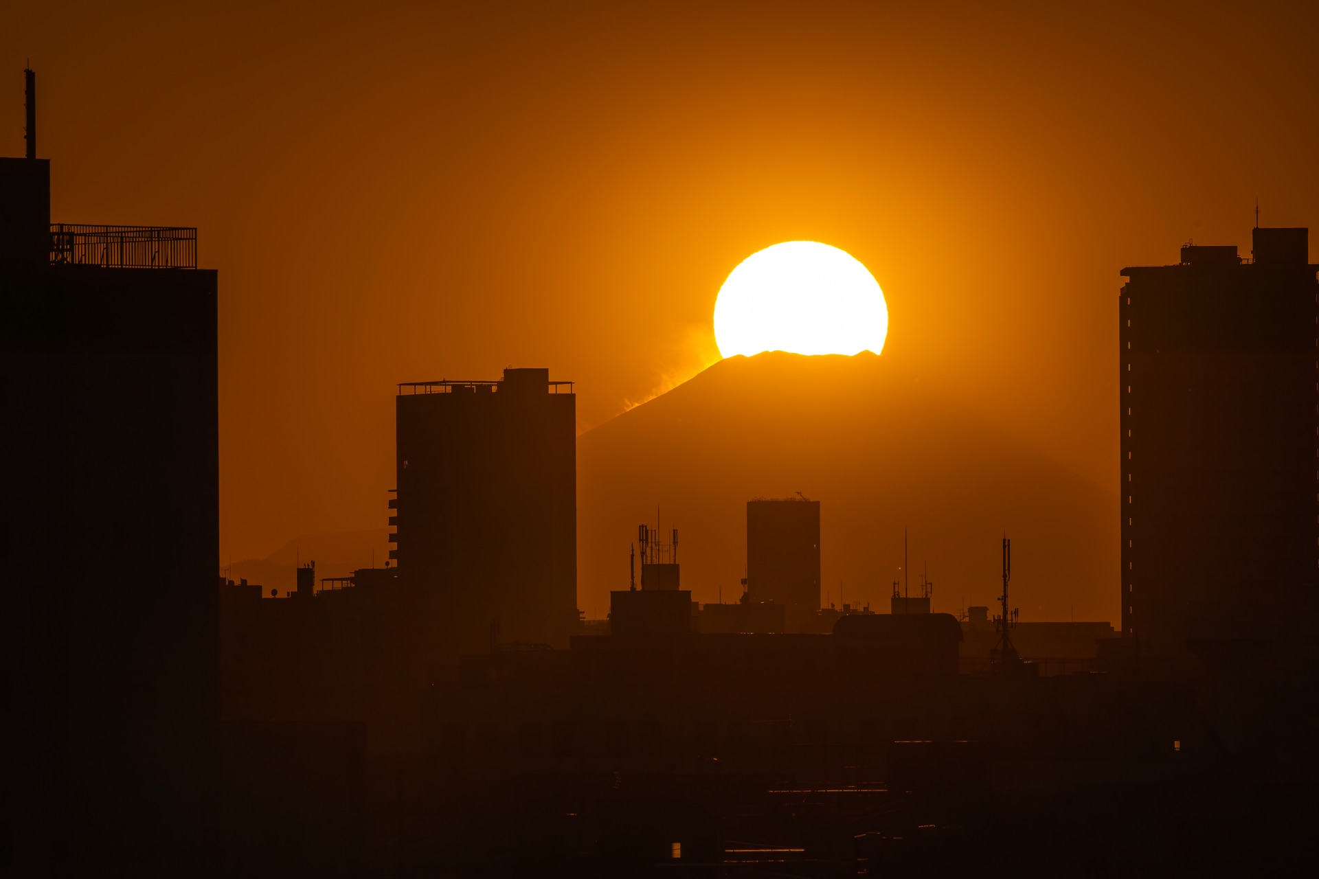 Diamond Fuji from Adachi-ku Tokyo with the sun setting behind buildings and Mt Fuji silhouette in the orange sky