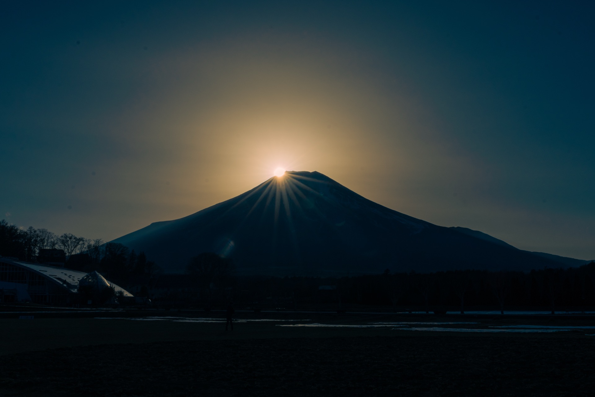 A wider view of Diamond Fuji with the sun on the summit and a foreground field with people watching