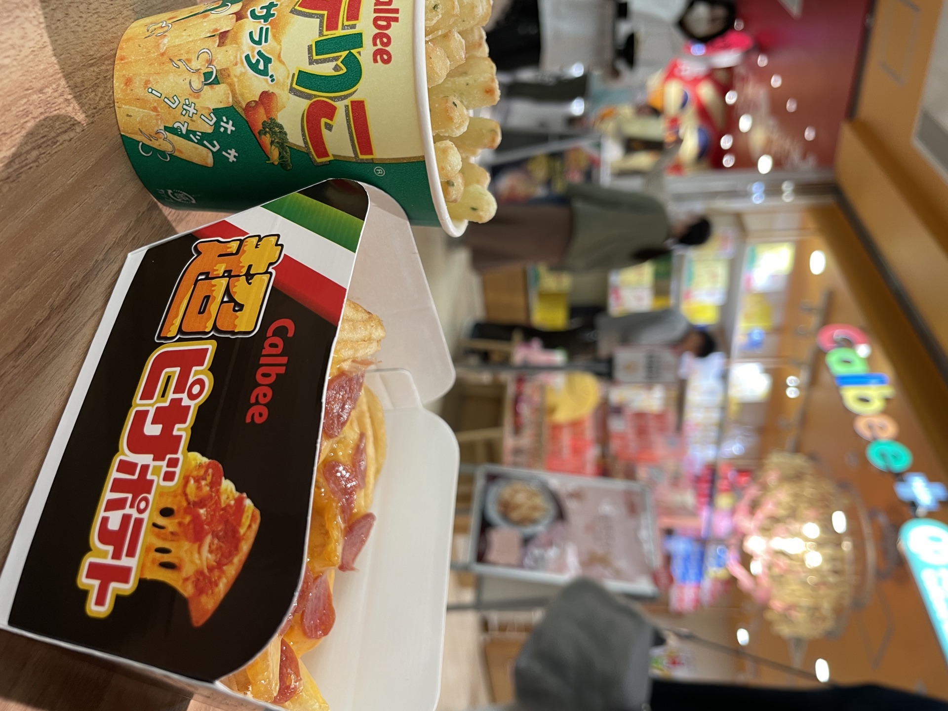 Hand holding Poteriko Salad cup and Pizza Potato box at Calbee+ Ebina SA