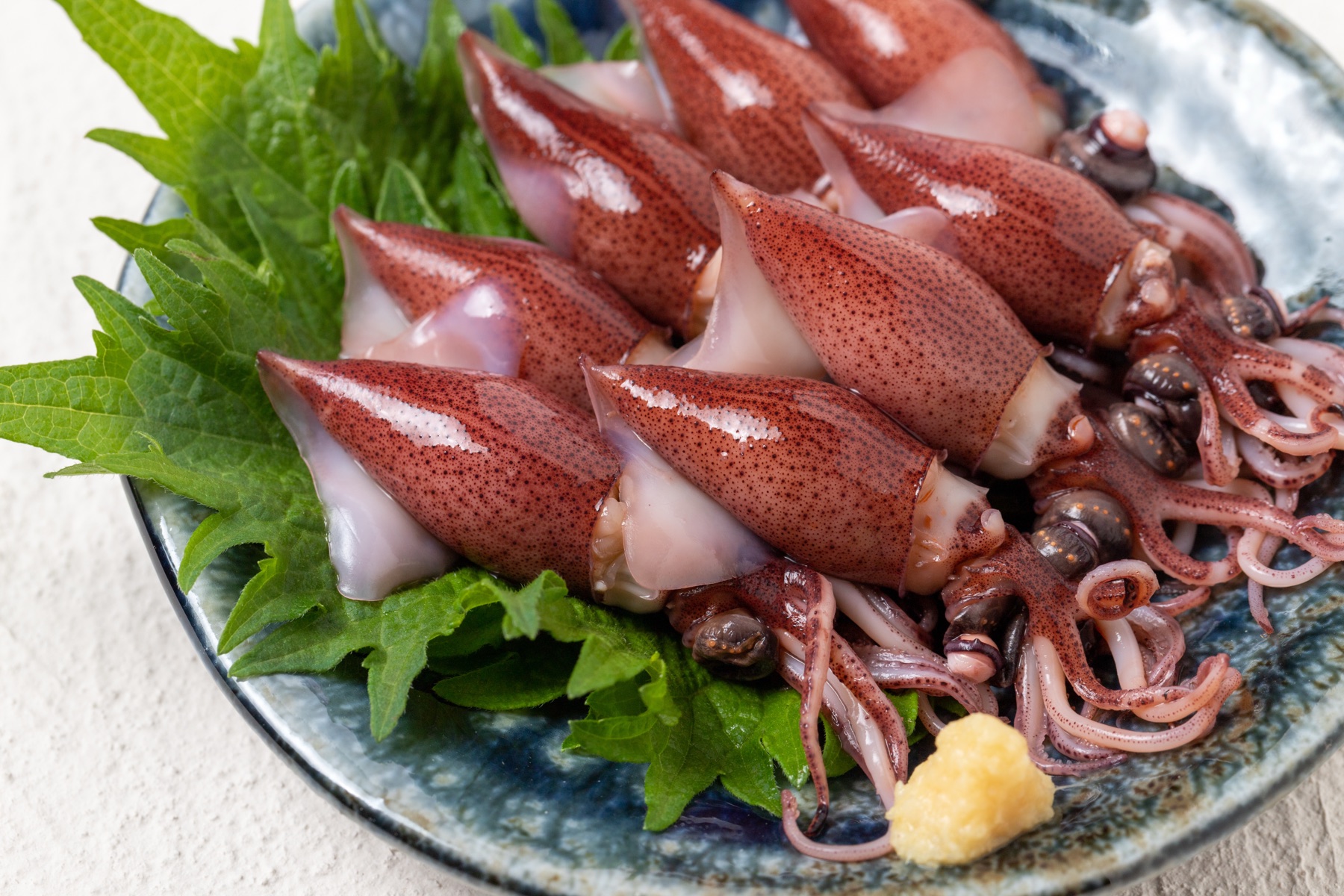 Plate of firefly squid, their reddish bodies arranged on green shiso leaves with a dab of ginger paste, the classic spring presentation of Toyama hotaruika.