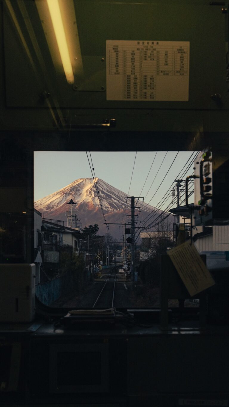 Mt Fuji with pink-red crimson alpenglow on its snow cap viewed through the front window of an early-morning Fujikyu Railway train, taken February 6 2026 at 6:48 AM JST from inside the Fujisan Station to Otsuki bound local train