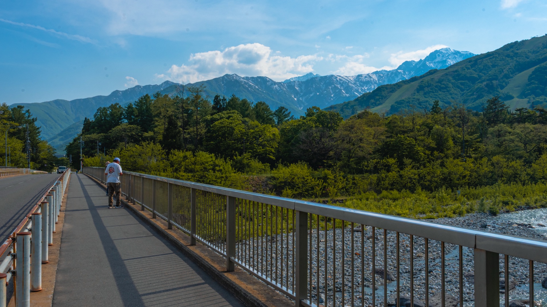 The walkway of Hakuba Ohashi bridge looking north with a pedestrian and mountain peaks in the distance