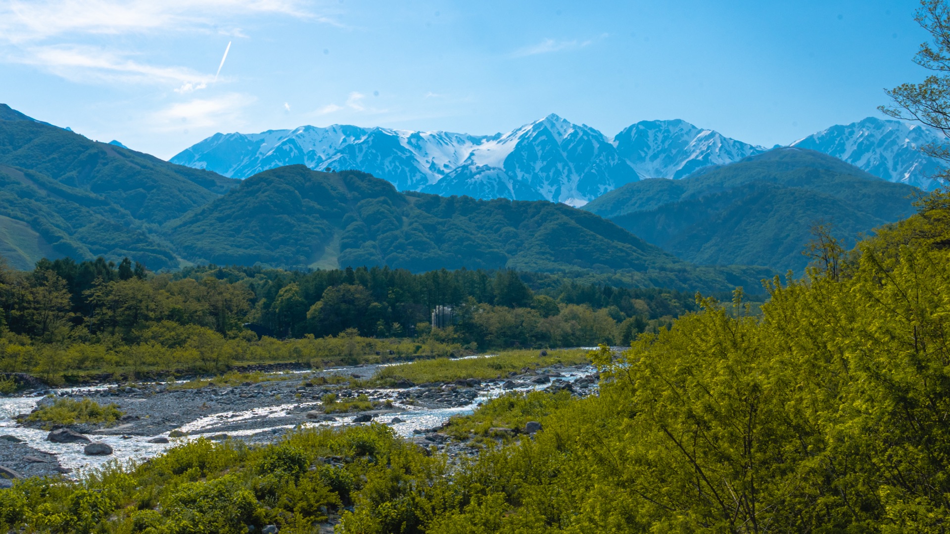 Wider composition of Matsugawa valley with Hakuba Sanzan peaks behind hills