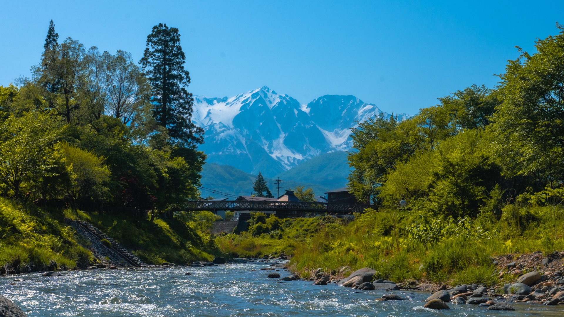 Suspension bridge at Hakuba Oide Park with snow-capped peaks visible behind