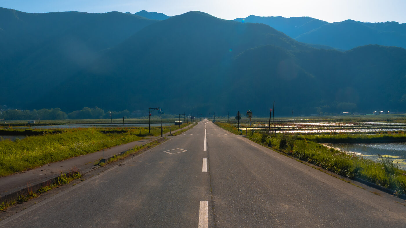 Empty rural road leading toward distant Hakuba mountains in low evening light